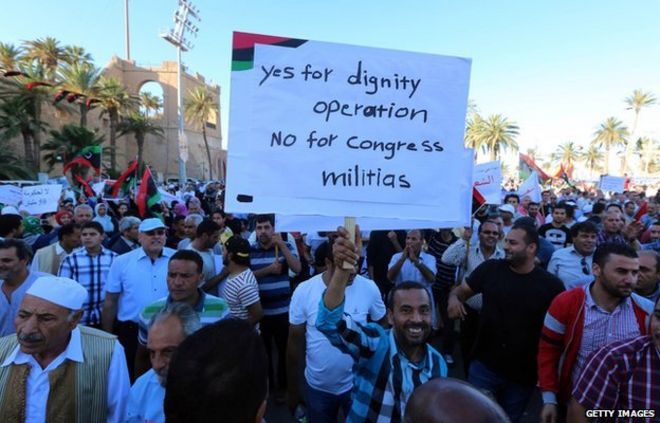 30 мая 2014 года в Триполи ливийцы держат плакаты и флаги во время митинга в поддержку бывшего генерала-изгоя, силы которого начали кампанию «достоинства» по разгрому ополченцев-джихадистов в восточной Ливии.