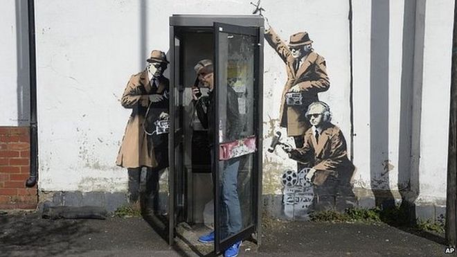 Человек в телефонной будке с произведениями искусства на стене позади