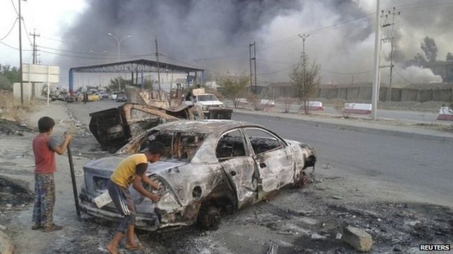 Иракские дети стоят рядом с транспортным средством, уничтоженным во время столкновений между суннитскими боевиками и иракскими силами безопасности в Мосуле (10 июня 2014 года)