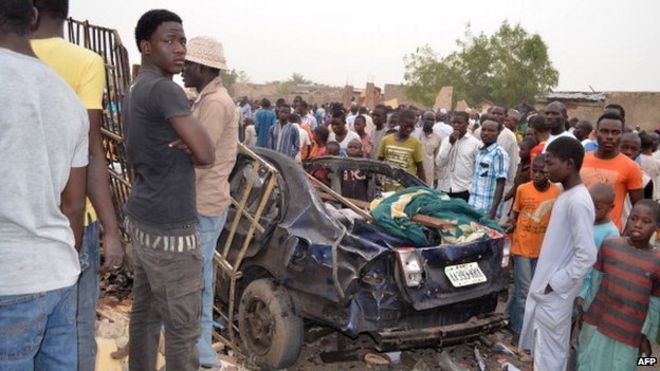 Люди смотрят на обломки автомобиля 2 марта 2014 года, после двух смертельных взрывов в многолюдном районе Майдугури, Нигерия