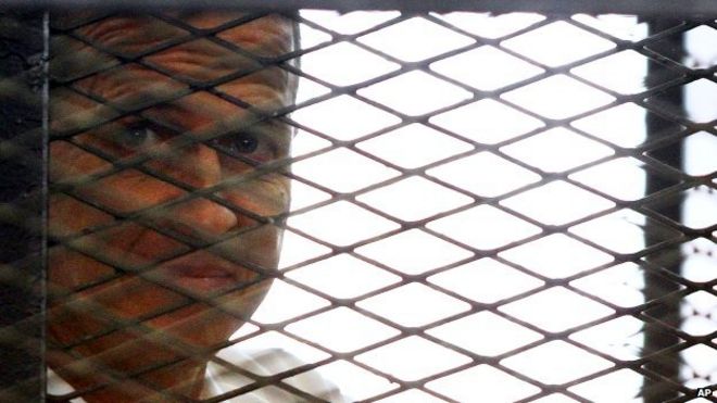 Журналист «Аль-Джазиры» Питер Гресте выглянул из клетки в зале суда в Каире, Египет - понедельник, 23 июня 2014 года
