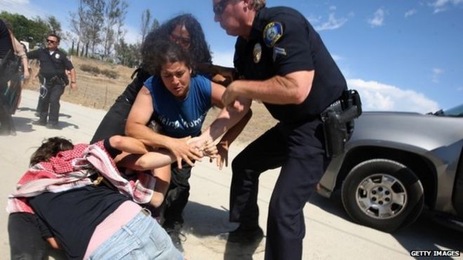 Противодемонстранты протестующих против прибытия автобусов, перевозящих в основном женщин и детей нелегальных мигрантов для обработки на пограничной патрульной станции Мурриета, столкновение с полицией в Мюриетта, штат Калифорния, 4 июля 2014 года