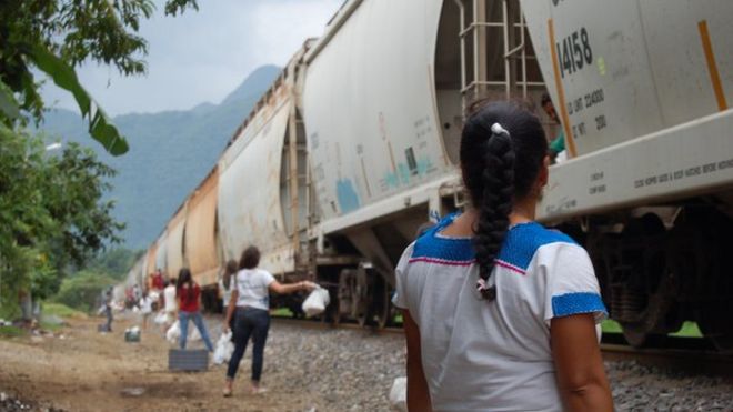 Женщины стоят у железнодорожных путей в Ла Патрона, готовых бросить еду мигрантам в поезде