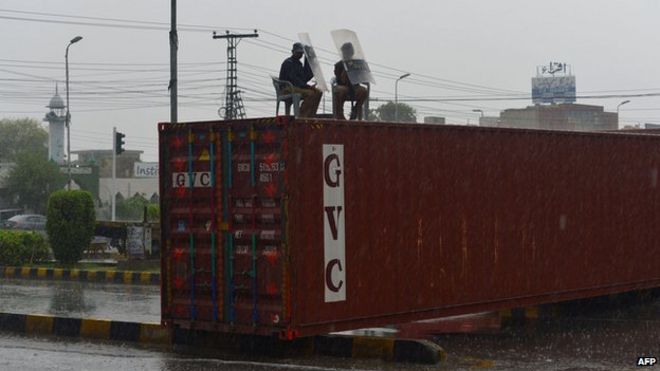 Пакистанские полицейские используют свои щиты, чтобы защитить себя от осадков, когда они сидят на контейнере возле дома лидера политической партии Пакистанского племени авами (ПАТ), канадского священнослужителя Тахир-уль-Кадри, в Лахоре 9 августа
