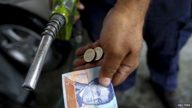 Рабочий на автозаправочной станции в Венесуэле показывает деньги, использованные для оплаты заправки бака