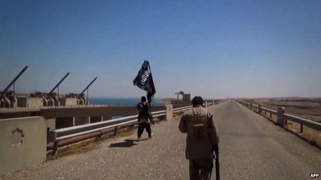 На снимке, предположительно, изображены боевики Исламского государства, размахивающие флагом джихадистов под торговой маркой, которые осматривают территорию плотины Мосула (9 августа 2014 года)