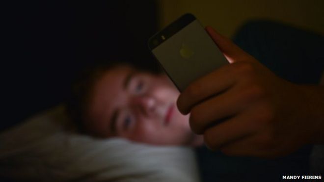 Человек проверяет телефон в постели