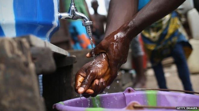 Житель моет руки в хлорированной воде в общественной ванной комнате в трущобах Вест-Пойнт 19 августа 2014 года в Монровии, Либерия