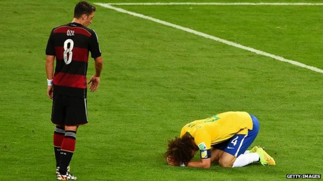 Давид Луис из Бразилии реагирует после поражения со счетом 7: 1 Германии, когда Месут Озил из Германии смотрит на чемпионат мира по футболу 2014 года в Бразилии