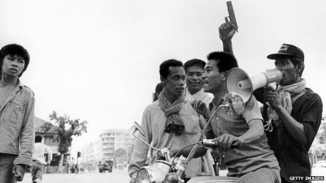 Солдат-кхмер-руж, держащий пистолет, едет на мотоцикле, в то время как 17 апреля 1975 года он и его товарищ въезжают в Пномпень