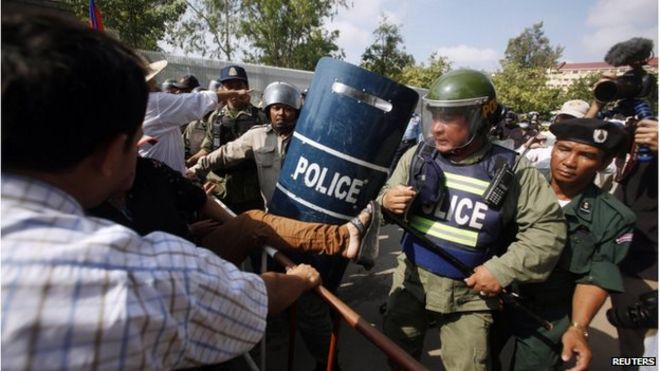 Протестующий избивает полицейского во время протеста против планов Камбоджи переселить перехваченных беженцев возле посольства Австралии в Пномпене 26 сентября 2014 года.