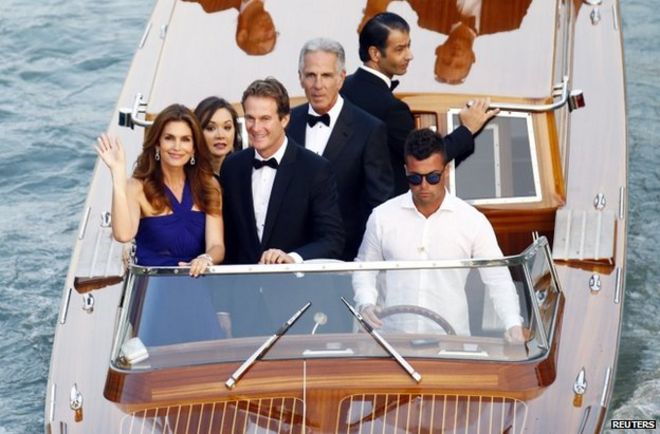 Модель Синди Кроуфорд (слева) машет рукой из лодки на Большом канале в окружении своего мужа, бизнесмена Ранде Гербера, 27 сентября