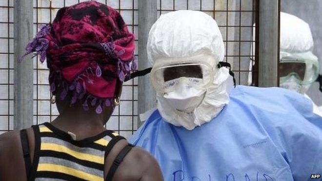 Медицинские работники в защитных костюмах приветствуют женщину, пришедшую доставить еду родственникам в больницу острова, где 30 сентября 2014 года в Монровии проходят лечение люди, зараженные вирусом Эбола