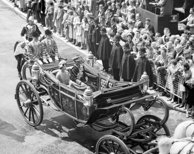 Улыбающиеся толпы на тротуаре и полицейские, одолеваемые от непогоды, приветствуют Короля Таиланда Пумипона и Королеву, когда они едут из Виктории в Букингемский дворец в начале его государственного визита в Лондон, 1960 год