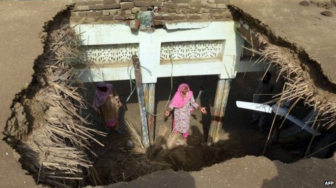 Пакистанская женщина показывает жестом под поврежденную крышу ее дома, предположительно вызванную снарядами, выпущенными индийскими войсками, в пограничной деревне Дхамала недалеко от восточного города Сиалкот в провинции Пенджаб