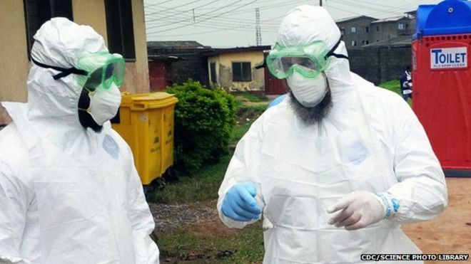 Врачи, носящие средства индивидуальной защиты вне отделения лечения Эболы в Нигерии