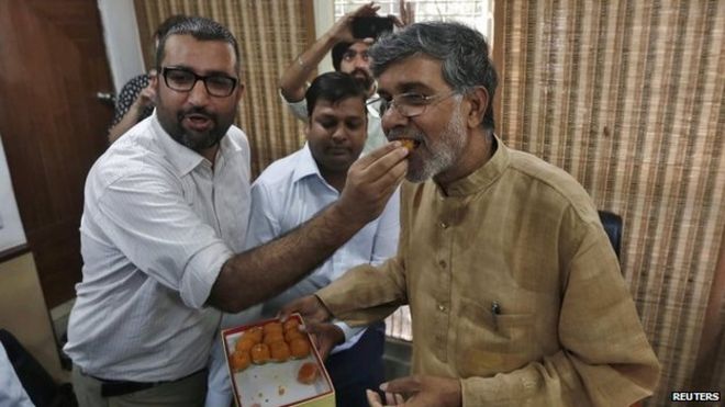 Индийскому активисту по защите прав детей Kailash Satyarthi (R) предлагают сладости доброжелатель в своем офисе в Нью-Дели 10 октября 2014 года.