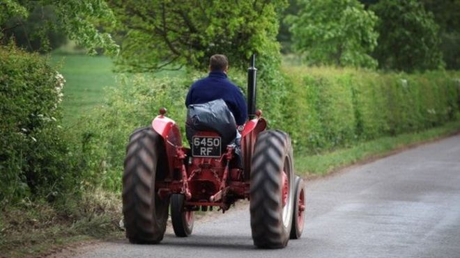 Один фермер ведет свой трактор по проселочной дороге в сельской местности Шропшира