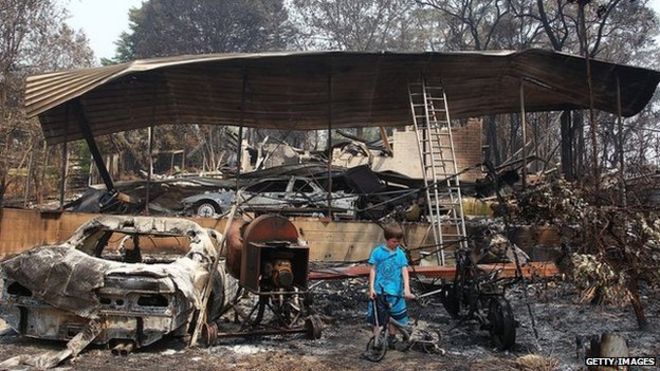 Мальчик осматривает остатки дома своего деда, который был разрушен лесным пожаром 21 октября 2013 года в Уинмали, Австралия