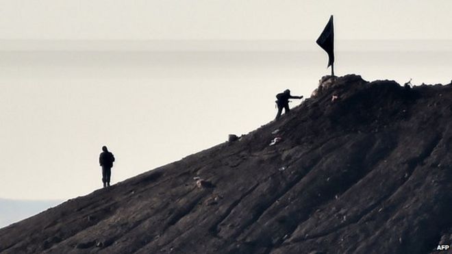 Предполагаемые боевики Исламского государства стоят возле черного флага IS возле турецко-сирийской границы
