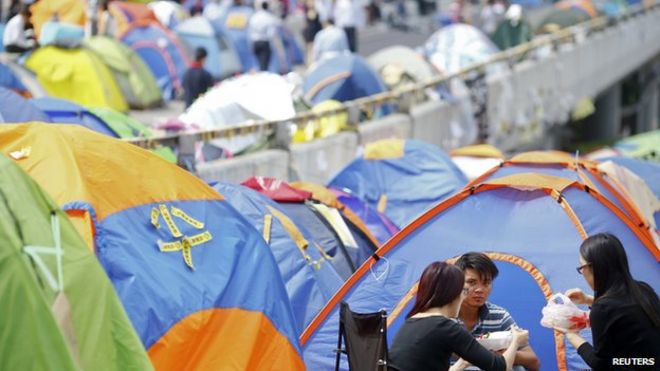 Люди обедают между палатками, установленными продемократическими демонстрантами в части финансового центрального района Гонконга, который протестующие занимают, 29 октября 2014 года