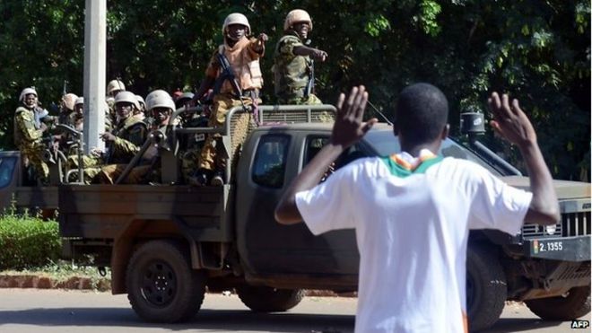 Мужчина жестом показывает, как военнослужащие буркинского происхождения прибывают в штаб-квартиру национального телевидения после того, как в районе Уагадугу были произведены выстрелы, 2 ноября 2014 г.