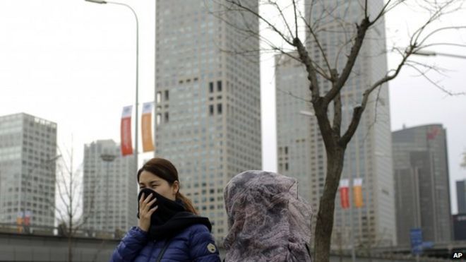Китайские женщины закрывают лицо платком, проходя мимо центрального делового района в Пекине, Китай. Вторник, 11 ноября 2014 г.