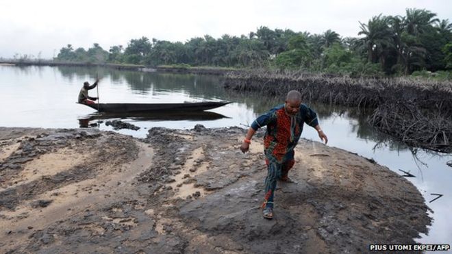 Мужчина ходит по скользкой сырой нефти по берегам и в водах болот дельты Нигера в Бодо, деревне в известном нигерийском нефтедобывающем Огониланде, где в июне в штате Нигерии находится река Шелл Петролеум Девелопмент Компани (SPDC), расположенная в штате Нигерии. 24, 2010.