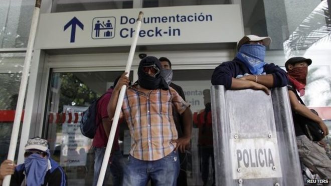 Протестующие в масках стоят возле аэропорта Акапулько 10 ноября 2014 года