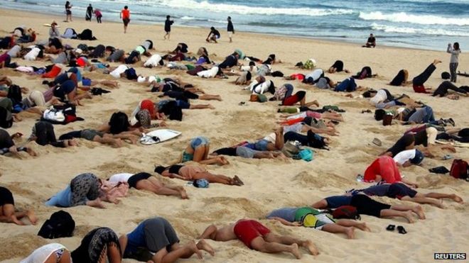 Группа демонстрантов принимает участие в акции протеста, закапывая головы в песок на пляже Бонди - 13 ноября 2014 г.