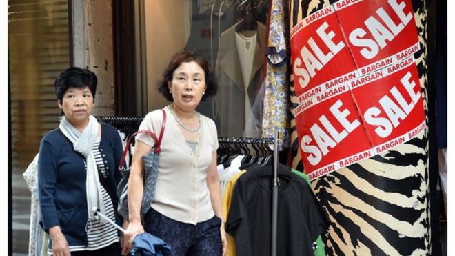 Люди проходят мимо одежды, выставленной возле магазина в Токио 29 августа 2014 года.
