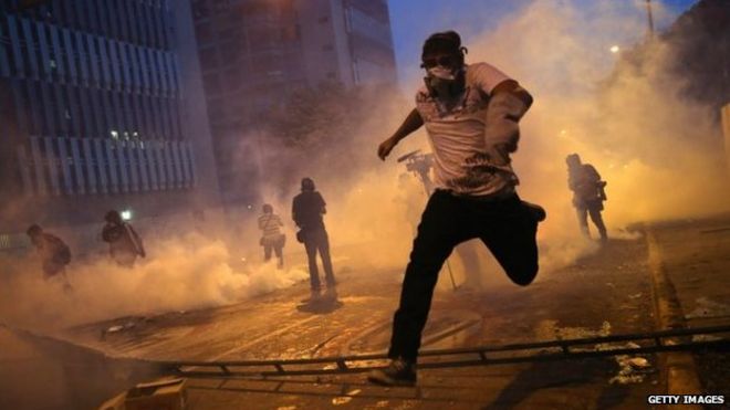 Протестующие бегут от слезоточивого газа, выпущенного венесуэльской национальной гвардией во время антиправительственной демонстрации 27 февраля 2014 года в Каракасе.