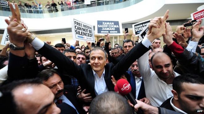 Экрем Думанли, главный редактор газеты Zaman, машет сотрудникам и сторонникам, будучи арестованным контртеррористической полицией в штаб-квартире газеты в Стамбуле.