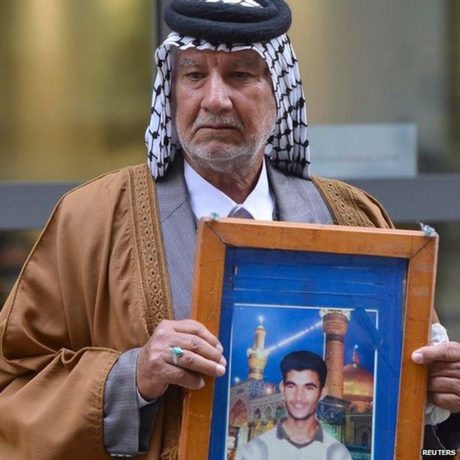 Мизал Карим аль-Суади держит фотографию своего сына за пределами расследования