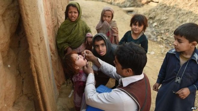 Пакистанский работник вакцинации против полиомиелита Шер Хан (C) вводит вакцину от полиомиелита ребенку в бедном районе, где 29 декабря 2014 года на окраине Исламабада находятся афганские беженцы и перемещенные внутри страны племенные люди