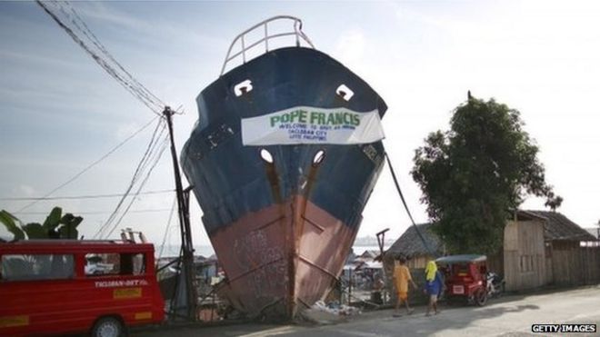 Приветственный знак для Папы Франциска украшает остатки корабля, застрявшего после тайфуна Хайян 15 января 2015 года в Таклобане, Лейте, Филиппины.