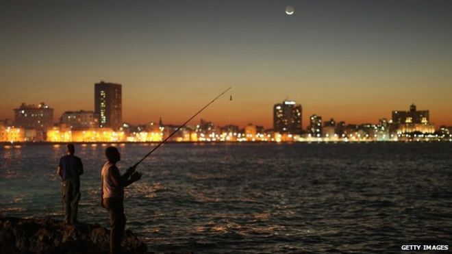 Мужчины ловят рыбу вдоль берега океана Малекон под луной ногтя в январе 2015 года в Гаване, Куба