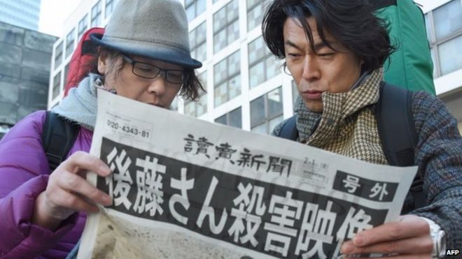 Люди читают специальное издание газеты в Токио после объявления о смерти Кендзи Гото