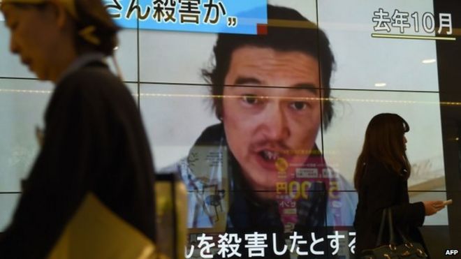 Люди проходят мимо большого экрана, сообщая, что Исламское государство убило заложника из Японии