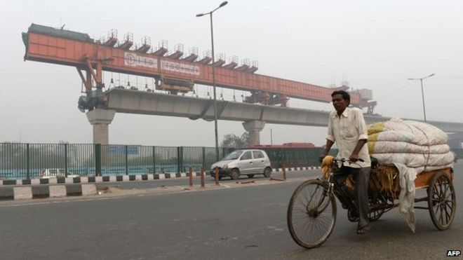 Индийский трехколесный рикша съемник проходит мимо строящегося надземного участка метро Дели в Нью-Дели.