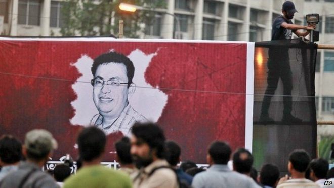 Бангладешский активист устанавливает свет на плакат с изображением портрета Авиджита Роя, когда другие собираются во время акции протеста против Роя в Дакке, Бангладеш, в пятницу, 27 февраля 2015 года.