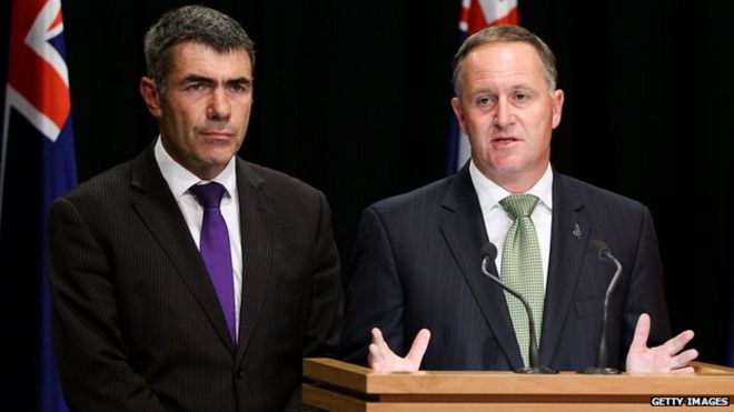 Премьер-министр Новой Зеландии Джон Ки беседует со СМИ, а министр первичной промышленности Натан Гай смотрит на здание парламента 10 марта 2015 года в Веллингтоне, Новая Зеландия.