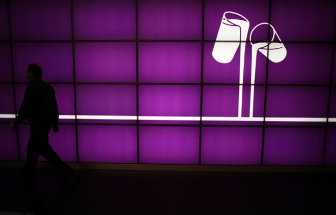 Сотрудник проходит мимо фиолетовой стены с логотипом Кэдбери о двух стаканах, наливающих молоко. На заводе компании Bournville.