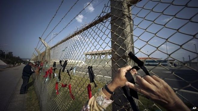 Демонстранты против перебазирования аэродрома Корпус морской пехоты США Футенма завязывают черные и красные ленточки на заборе американской базы Кэмп Шваб возле места планируемого переселения в Наго, префектура Окинава. Понедельник, 23 марта 2015 г.
