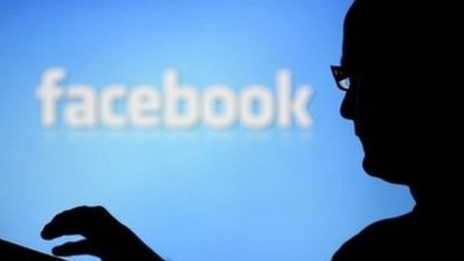 A man with a laptop is silhouetted against a screen with a Facebook logo in the background 14 August 2013