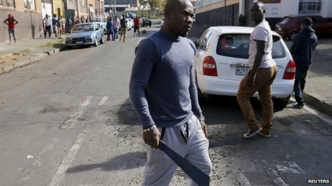 Африканский иммигрант держит мачете перед тем, как его разогнали сотрудники полиции в Йоханнесбурге, 17 апреля 2015 года