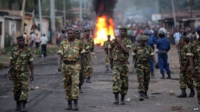 Бурундийские солдаты идут возле горящей баррикады, установленной протестующими, когда 27 апреля 2015 года люди протестуют против предложения президента о третьем сроке у власти в Мусаге, на окраине Бужумбуры