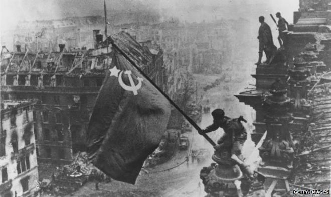 Солдат Красной Армии поднимает советский флаг над Рейхстагом в Берлине
