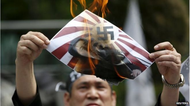 Активист против Японии сжигает плакат с изображением премьер-министра Японии Синдзо Абэ со свастикой на флаге восходящего солнца во время антияпонского митинга перед посольством Японии в Сеуле, Южная Корея, 28 апреля 2015 года