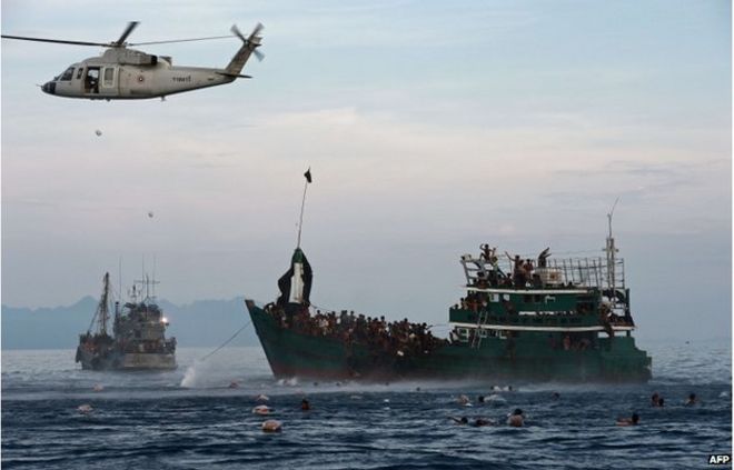 На этом снимке, сделанном 14 мая 2015 года, изображены мигранты рохинджа, плавающие для сбора продовольствия, сброшенного вертолетом тайской армии после того, как они прыгнули с лодки (R), дрейфующей в тайских водах у южного острова Ко Липе в Андаманском море.